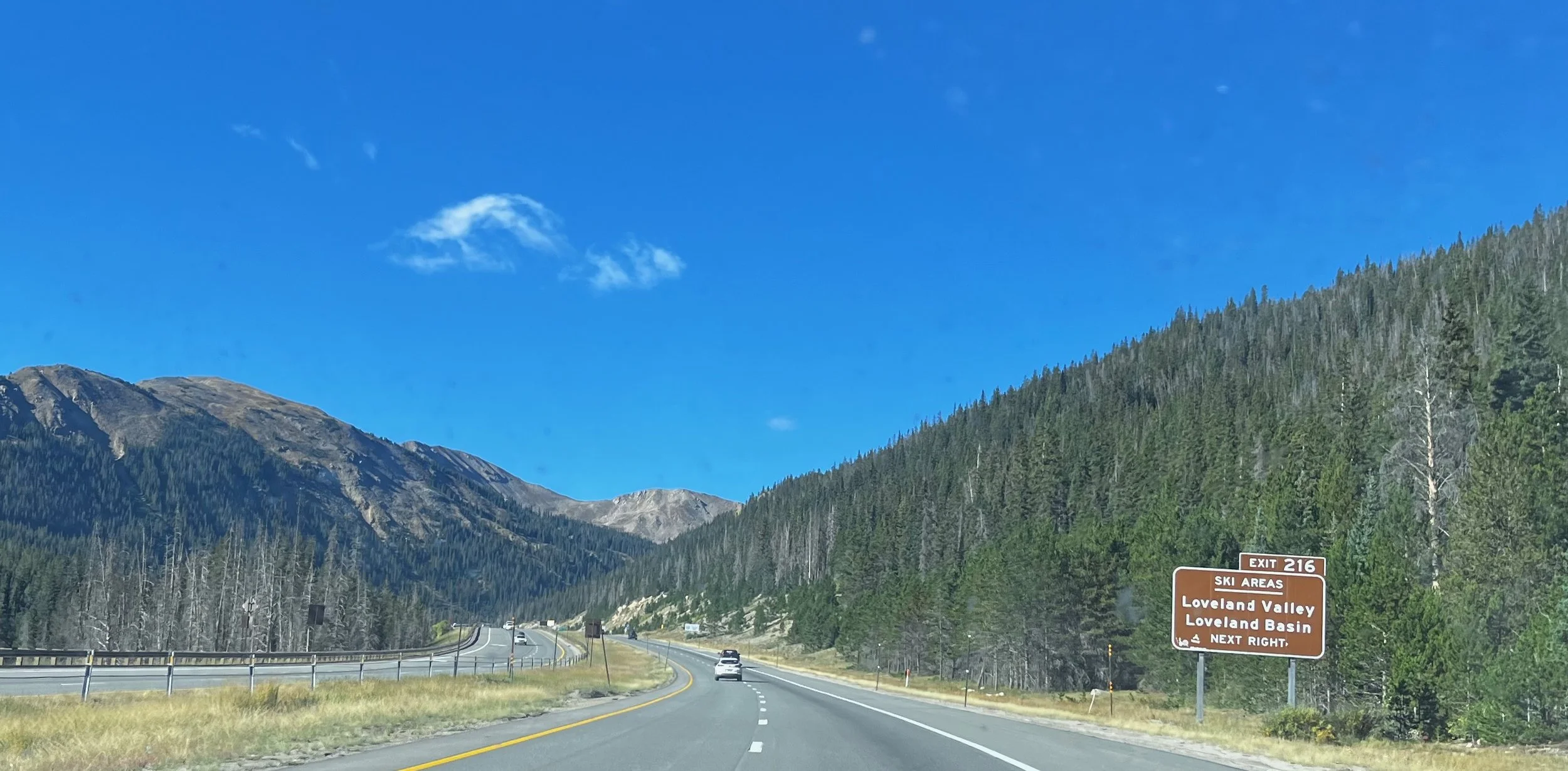 Interstate 70 curves through the mountains near Loveland Pass, Colorado, with a sign for the Loveland Pass exit beside the road.