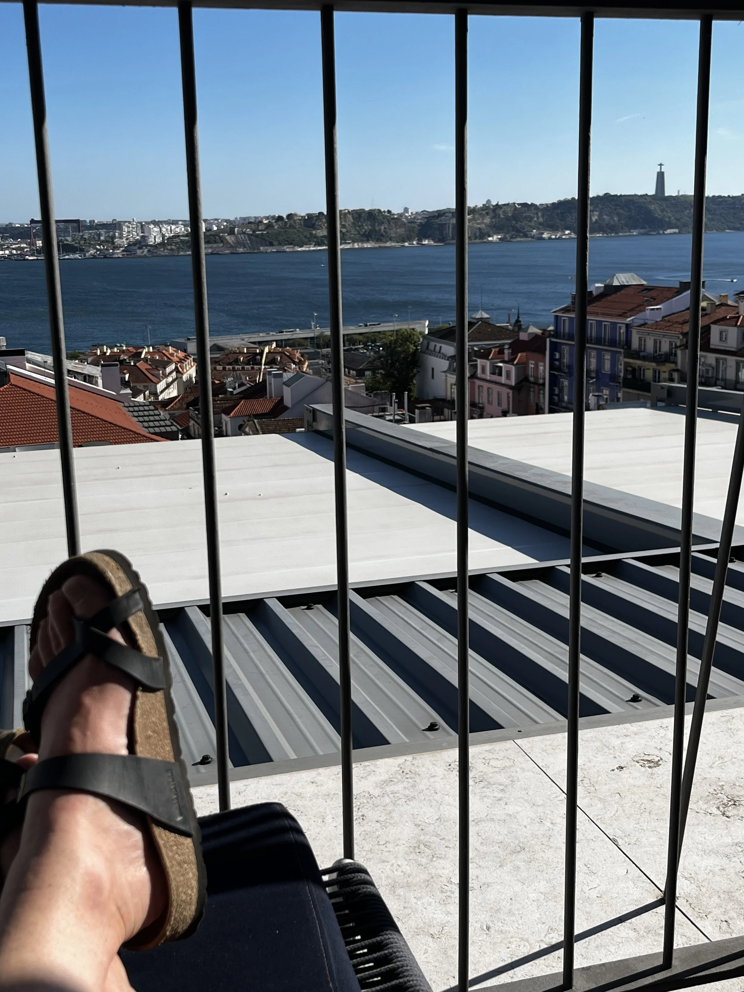 View from a Lisbon rooftop bar across the Tagus River toward Almada and the Cristo Rei monument.
