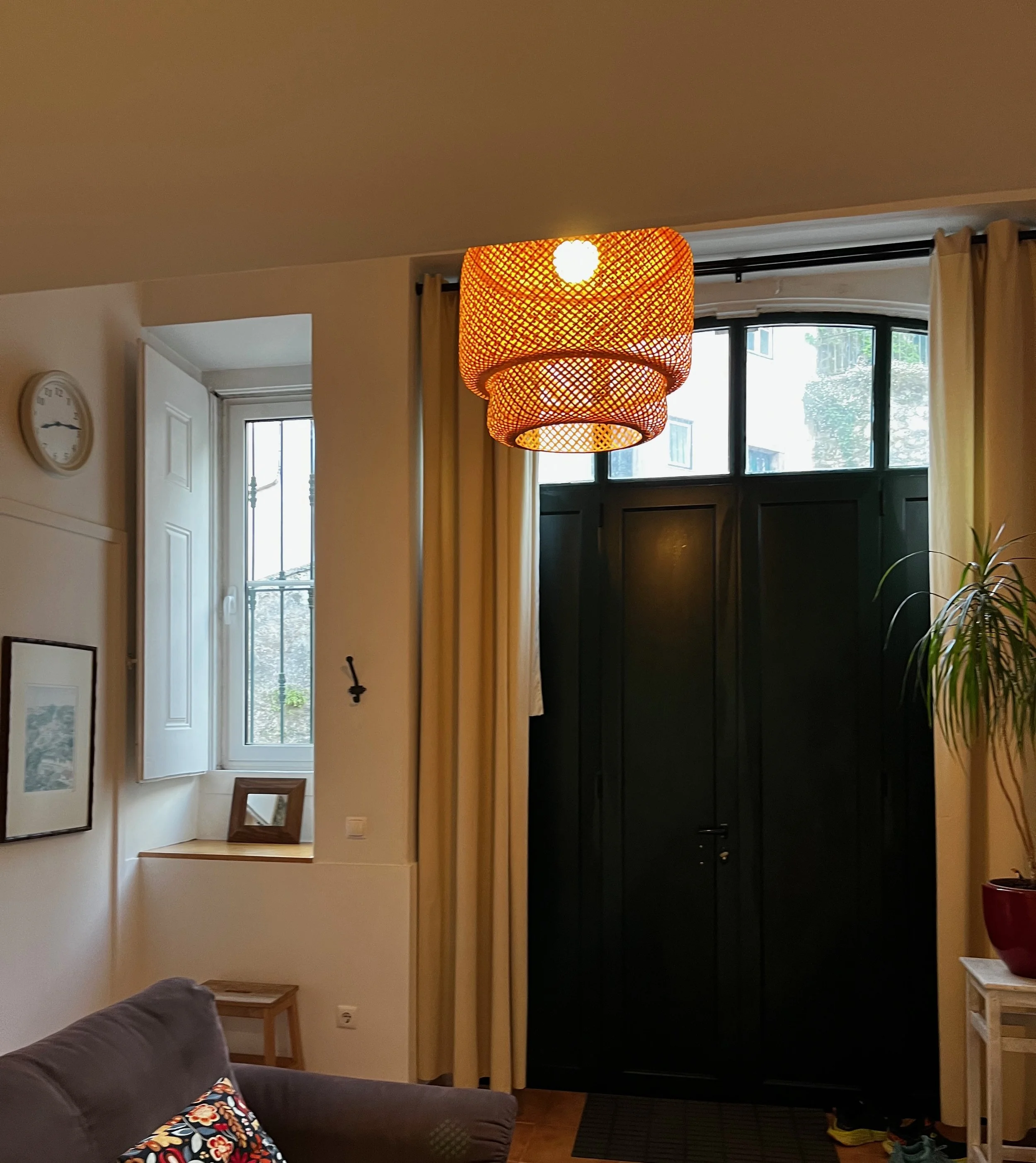 Interior View of a Living Room with a black front door, window, beige curtains, and a hanging orange woven lampshade.