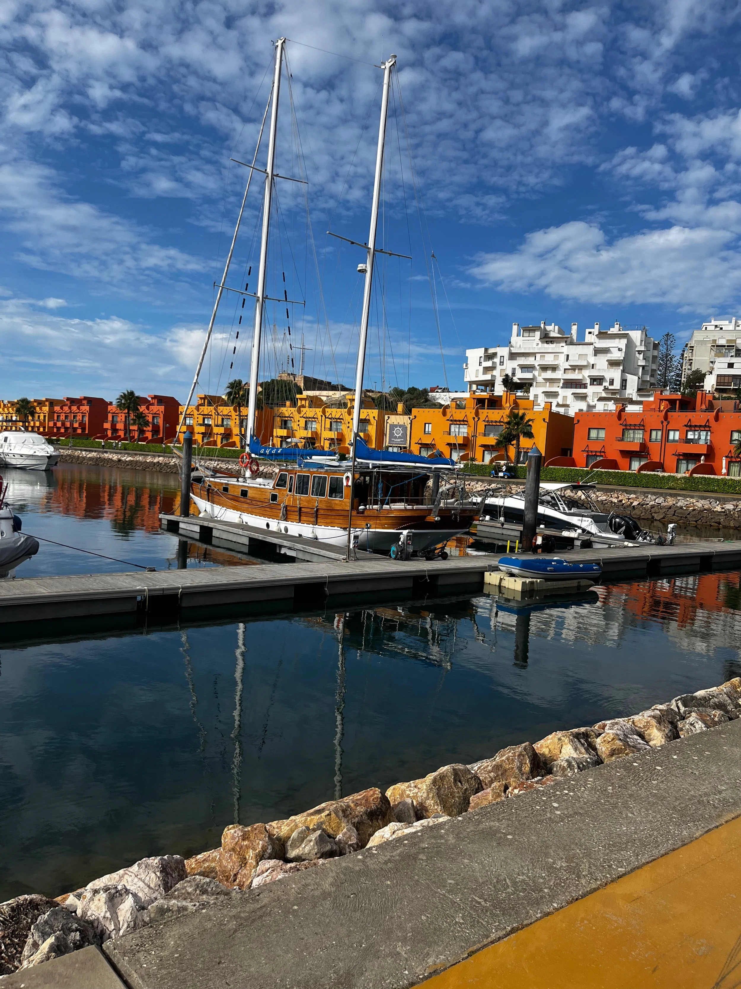 boats docked at a marina with colorful condos in the background under a partly cloudy blue sky.