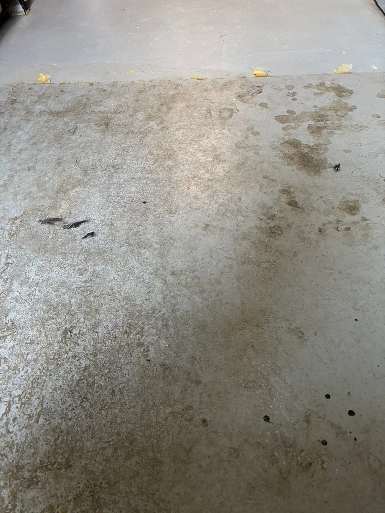 Concrete floor with dirt, water stains, and small debris, near a concrete step.