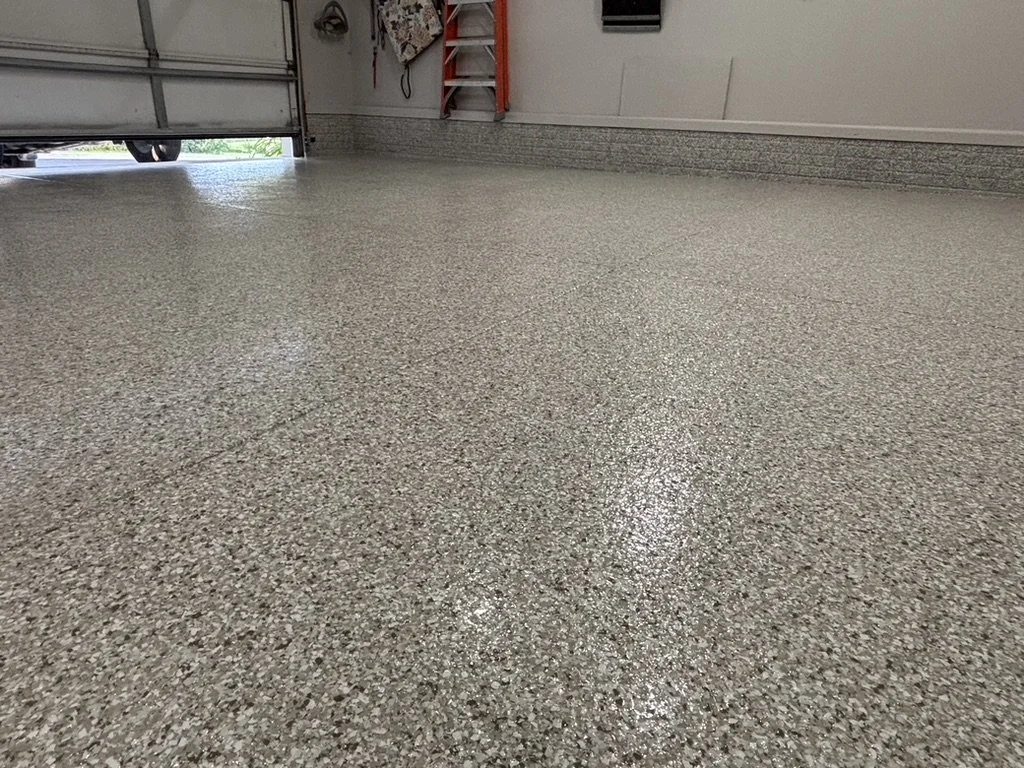 Smooth, polished concrete garage floor with a small portion of a garage door open, revealing outdoor greenery.