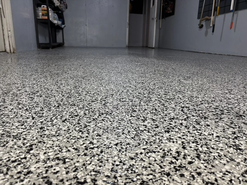 Polished speckled gray and black epoxy garage floor with tools hanging on the wall and a small shelving unit in the background.