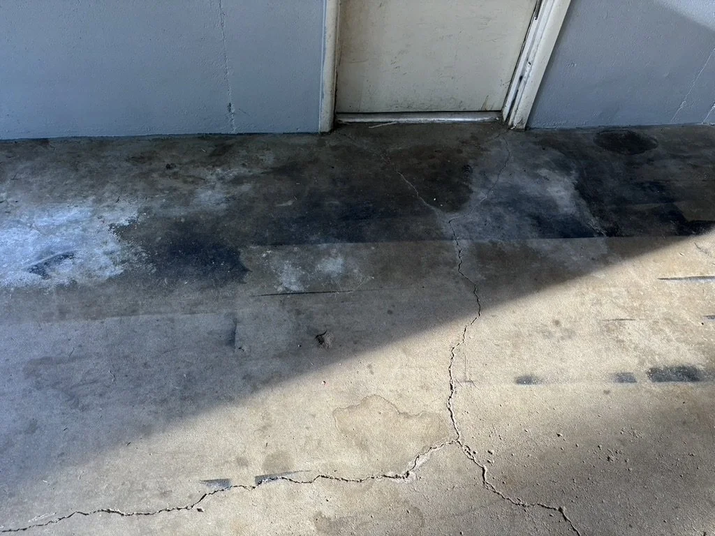 Concrete floor with cracks and stains in front of a closed door.