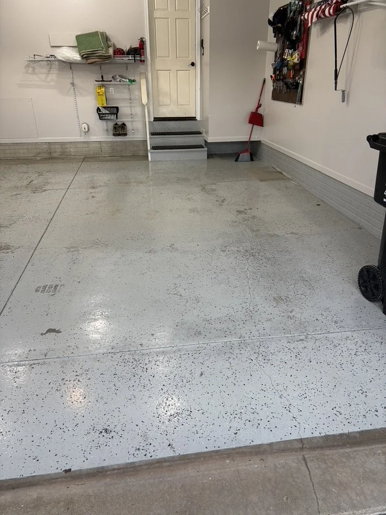 Empty garage with a polished concrete floor, a step ladder leading to a door in the back, and tools hanging on a wall organizer on the right.