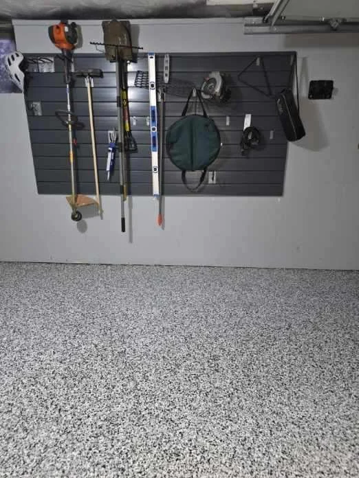 Tools hanging on a wall in a garage, including a chainsaw, rake, level, and other gardening or construction tools.