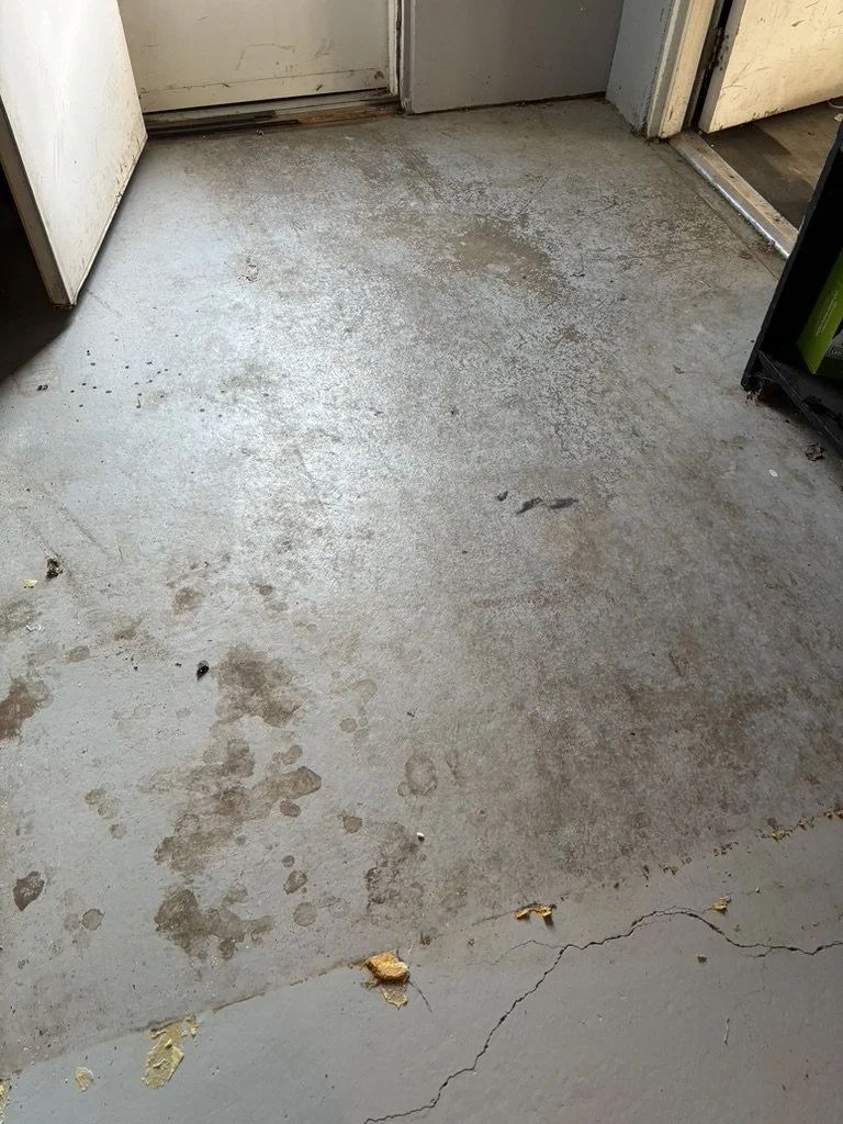 Concrete floor near a door with stains, dirt, cracks, and debris.