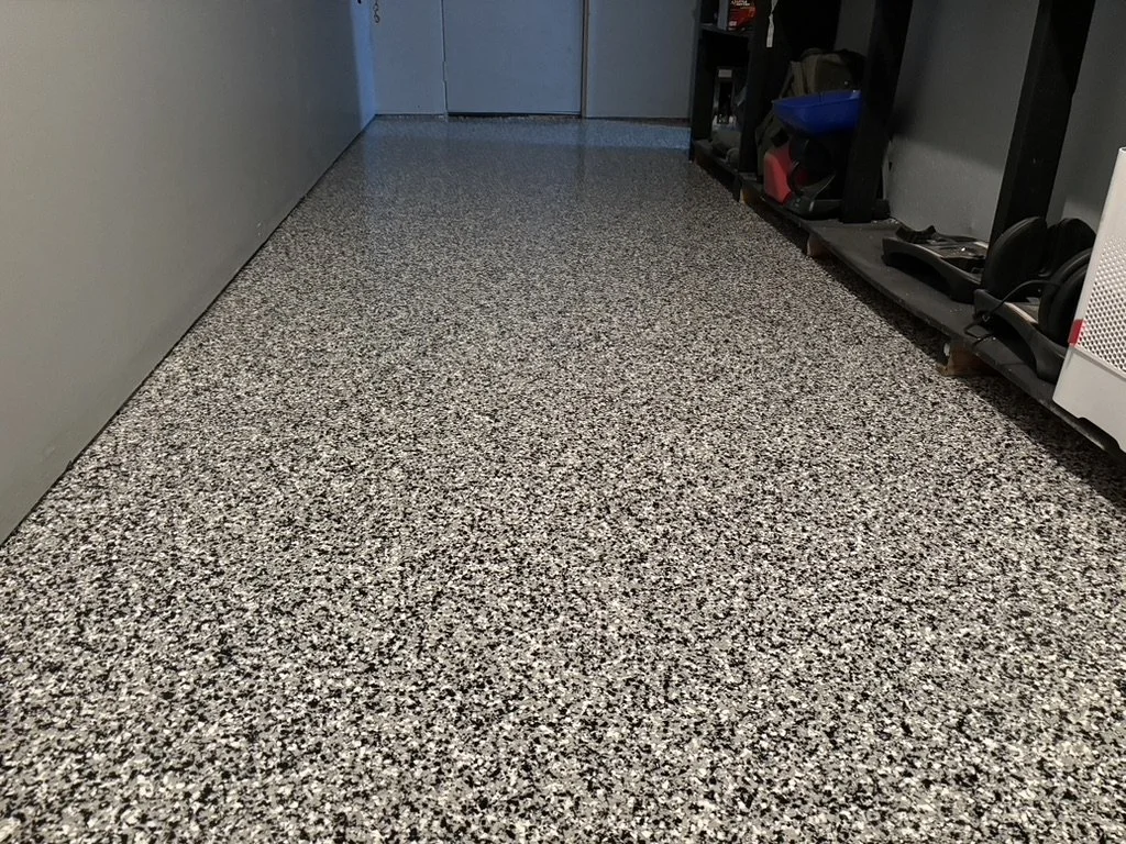Indoor utility room with gray speckled epoxy floor, shelves with various tools and equipment, and a closed blue door at the back.