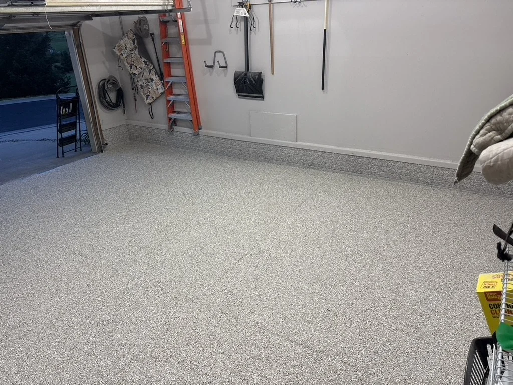 Empty organized garage with tools hanging on the wall, a ladder, a chair outside, and storage items.