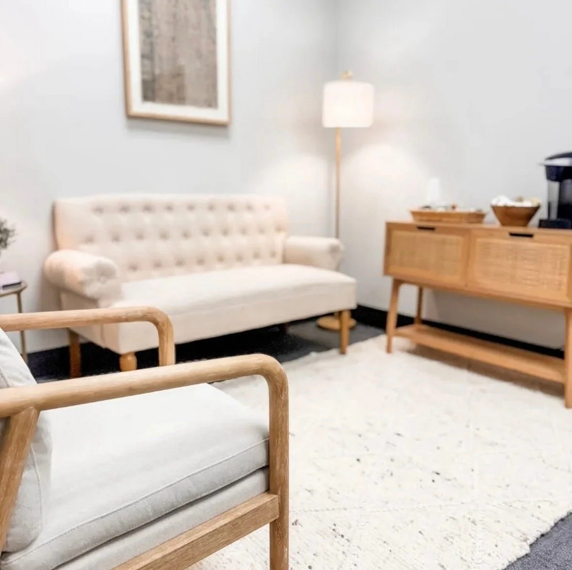Living room with beige sofa, wooden armchair, wooden cabinet, white rug, floor lamp, and wall art.
