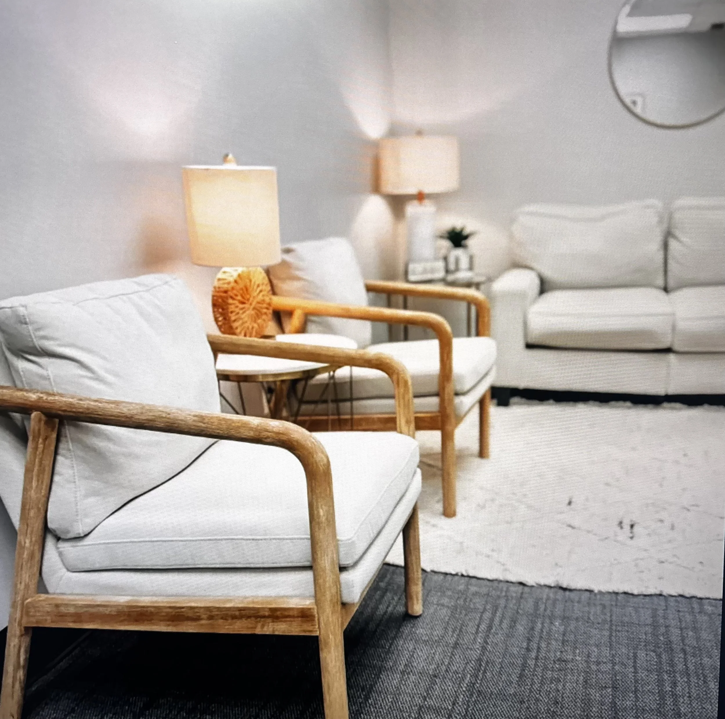 Living room with white sofas, wooden armchairs, side tables with lamps, a rug, a small plant, and wall decor.