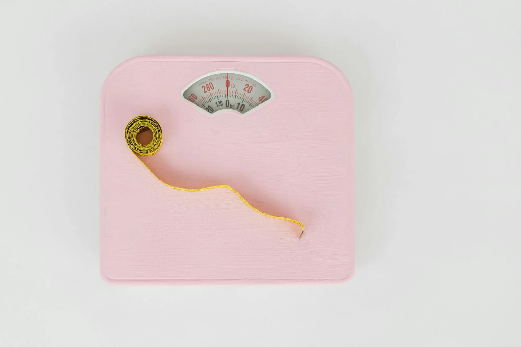 Pink bathroom scale with a yellow measuring tape placed on top.