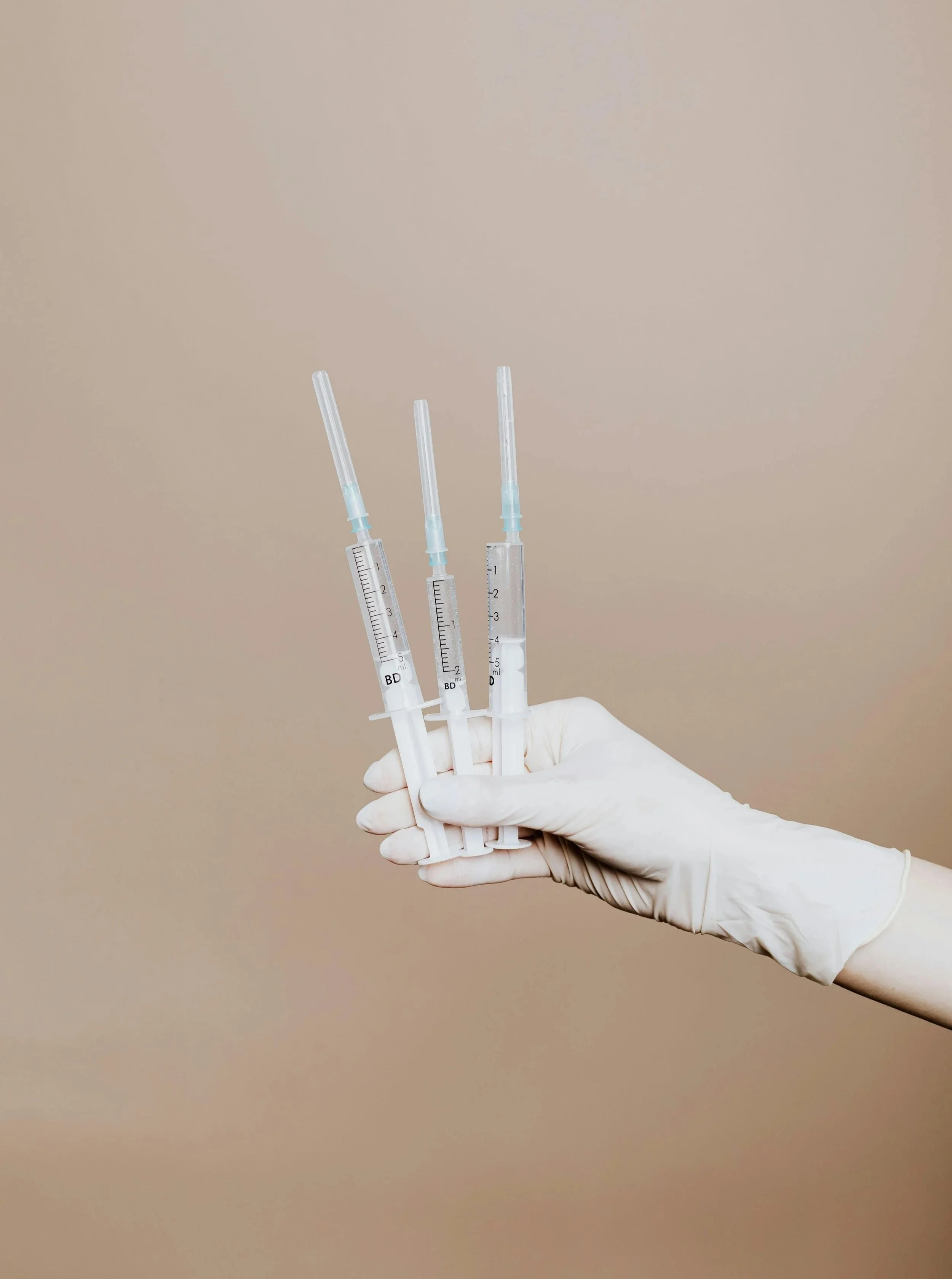 Gloved hands holding 3 medical aesthetic syringes.