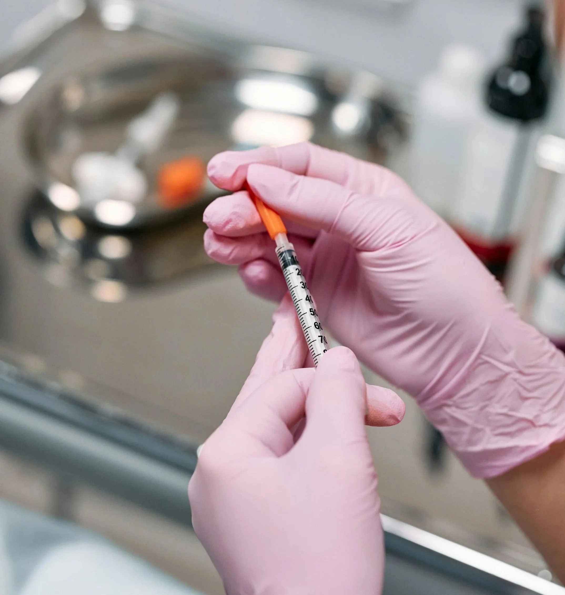 Gloved hands taking the cap off of an aesthetic injector syringe.