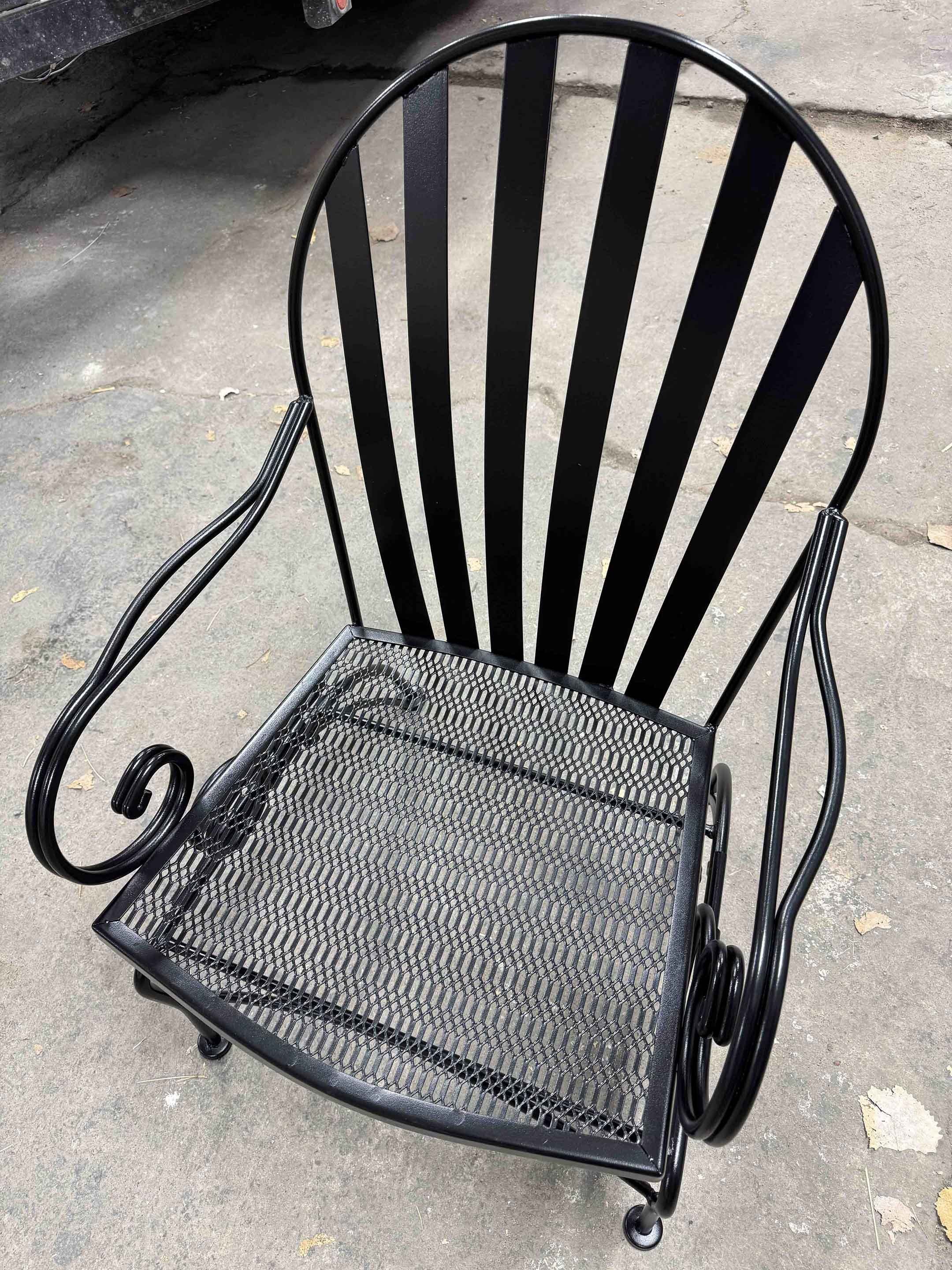 Black metal chair with a slatted backrest and mesh seat on a concrete surface.