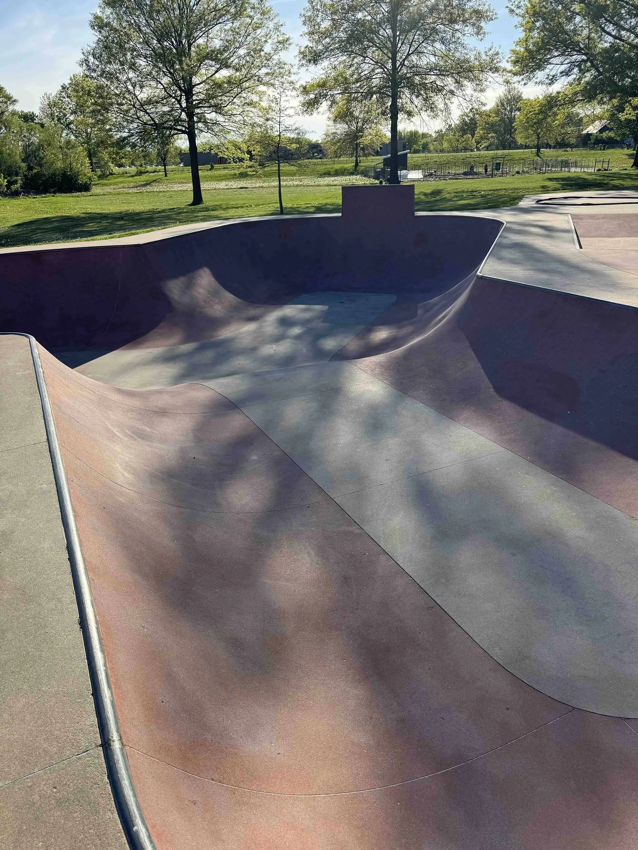 Empty skate park bowl with trees and grass in the background on a sunny day.