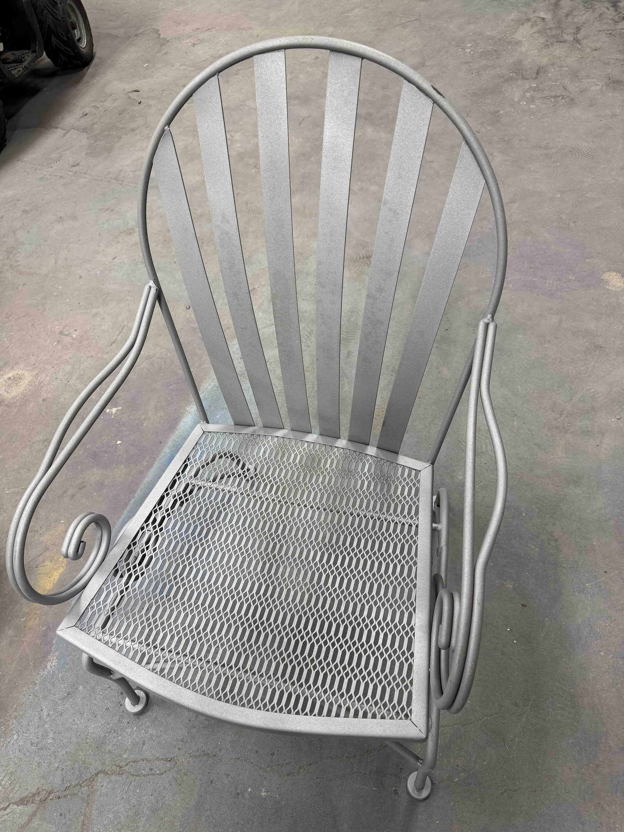 Metal outdoor chair with a curved back and armrests, featuring a mesh seat, placed on a concrete floor.