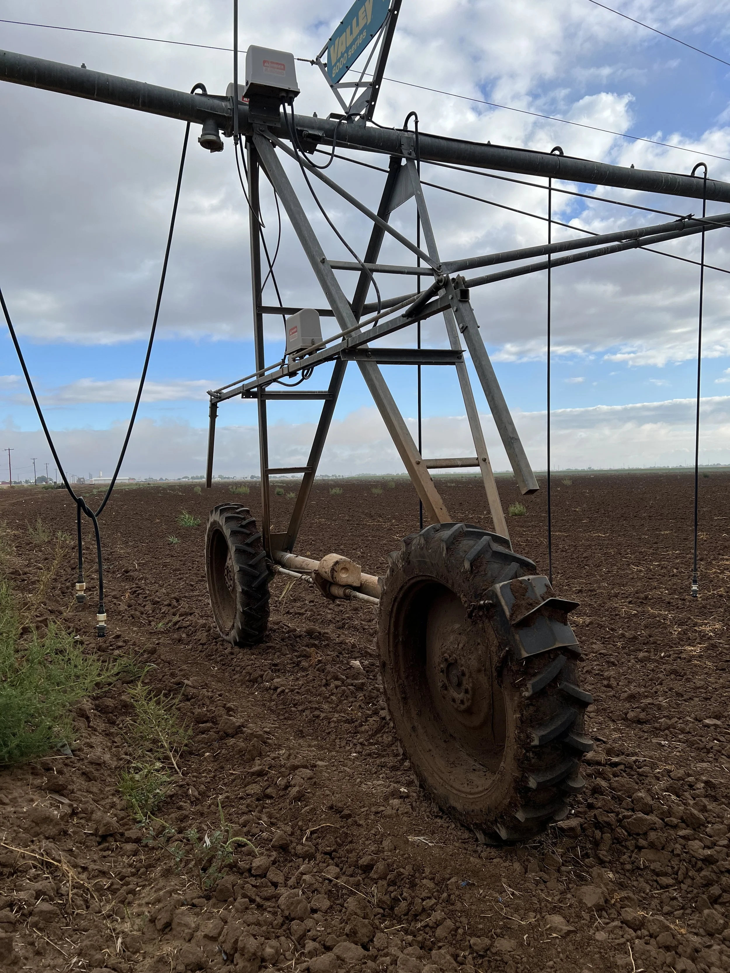 An irrigation system in a farm field with large rubber tires and metal framework, under a partly cloudy sky.