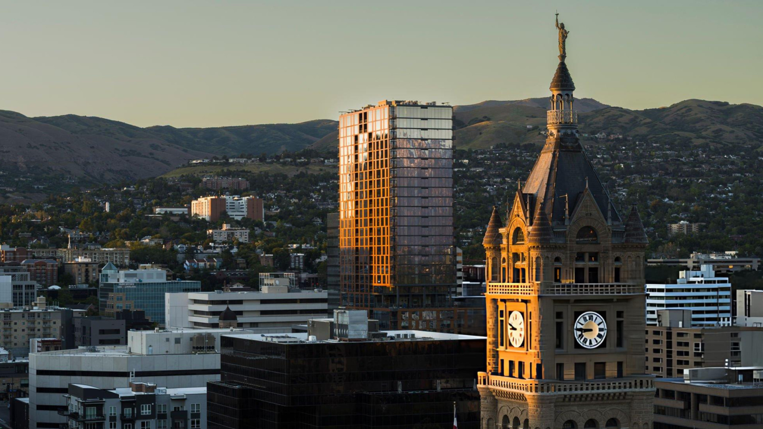 Salt Lake City and County Building clock tower glowing in golden evening light with downtown Salt Lake City and mountain views in the background, Utah.