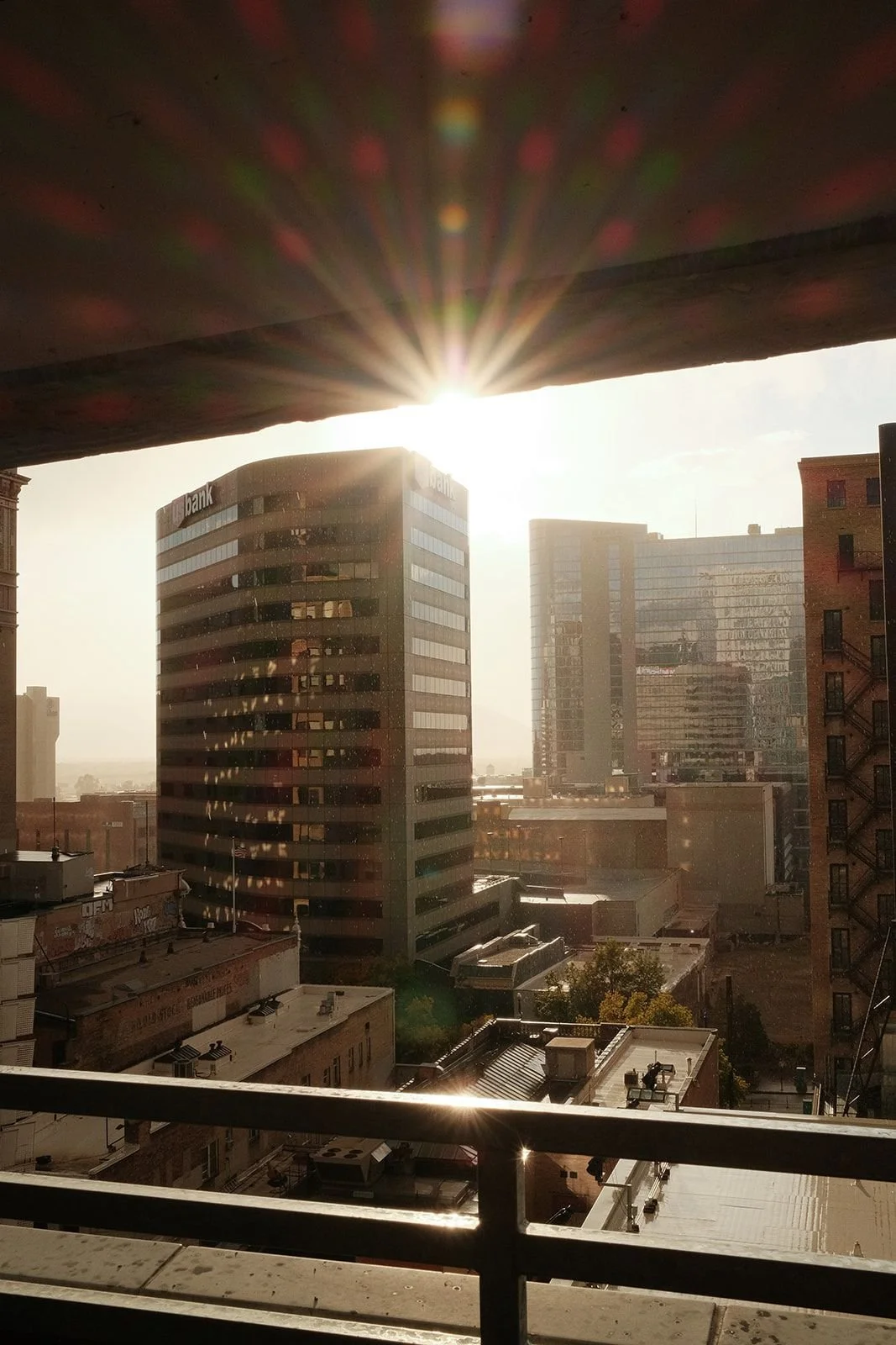 Sunburst over the Salt Lake City skyline and US Bank building, viewed from a balcony at golden hour.