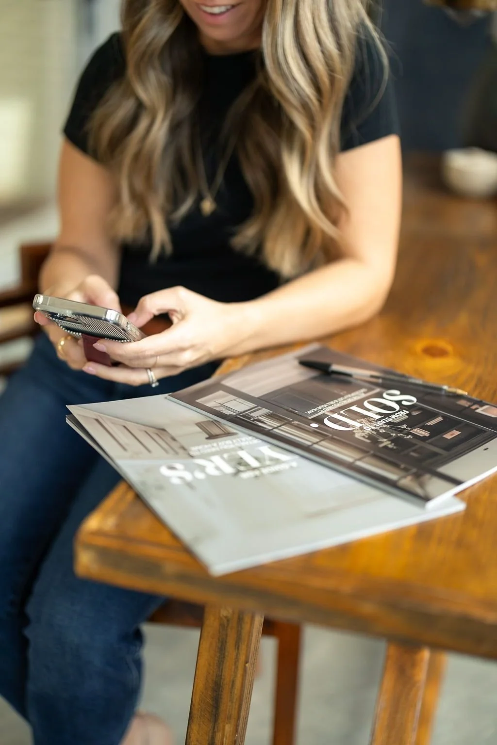 Close-up of Britt Kershner's hands holding a phone next to real estate guides titled "Sold" and "Buyer's."