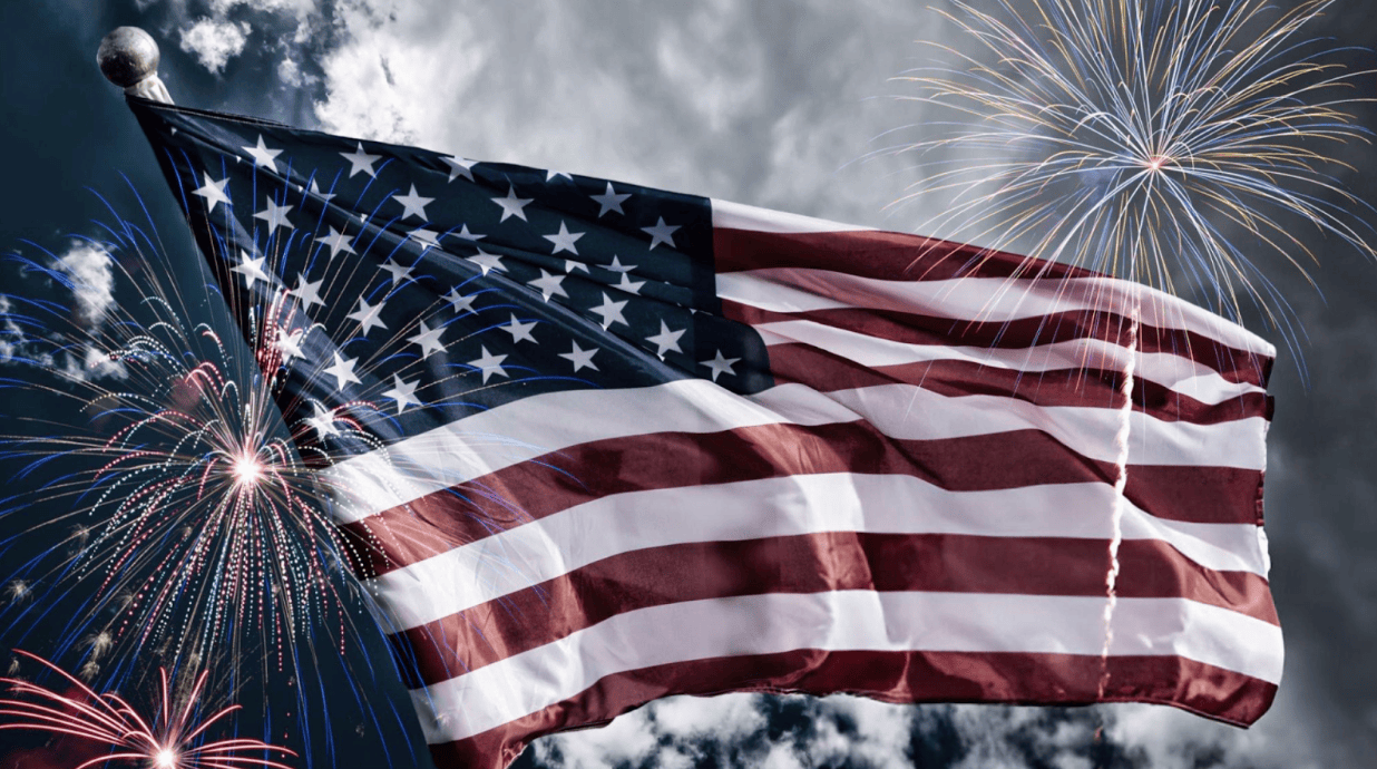 A waving American flag in the sky with fireworks going off around it.