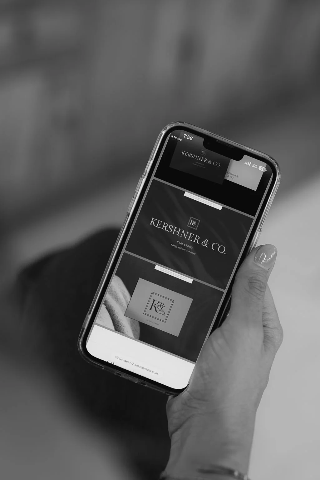 Female hand holding an iPhone with Kersher & Co.'s logos on the screen.