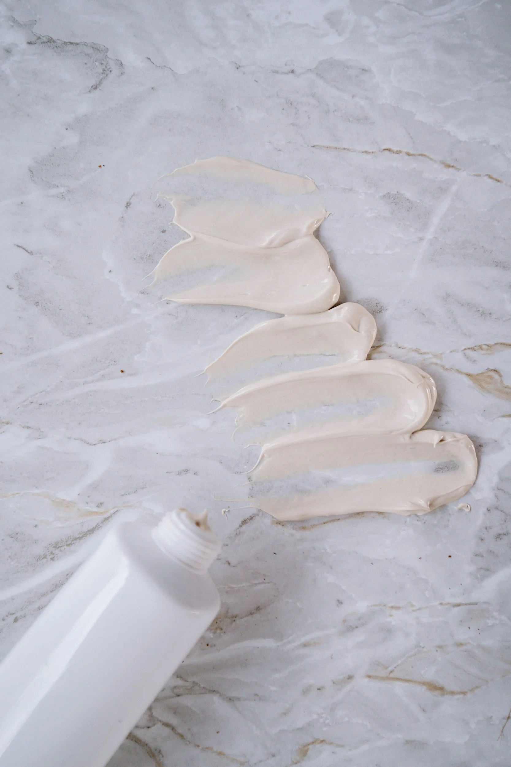 White cream being squeezed out of a tube onto a light-colored marble surface.