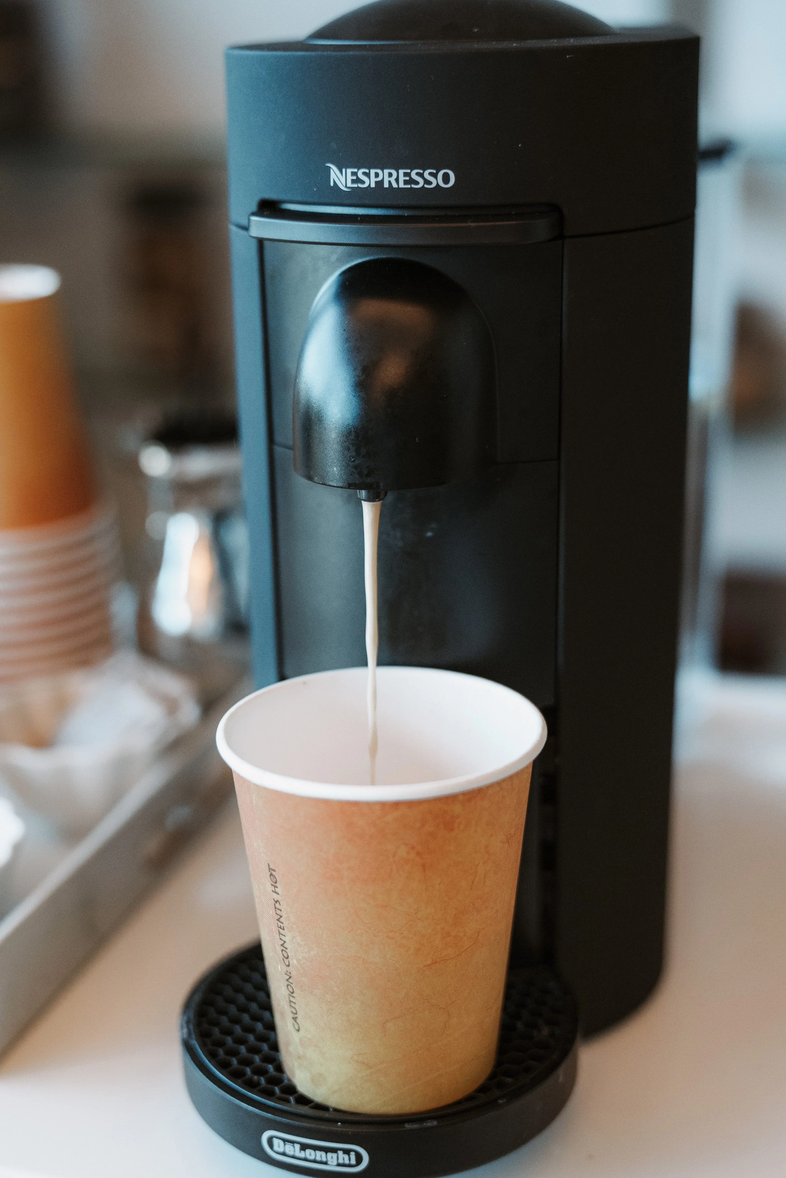 A black Nespresso coffee machine brewing coffee into a paper cup on a kitchen countertop.