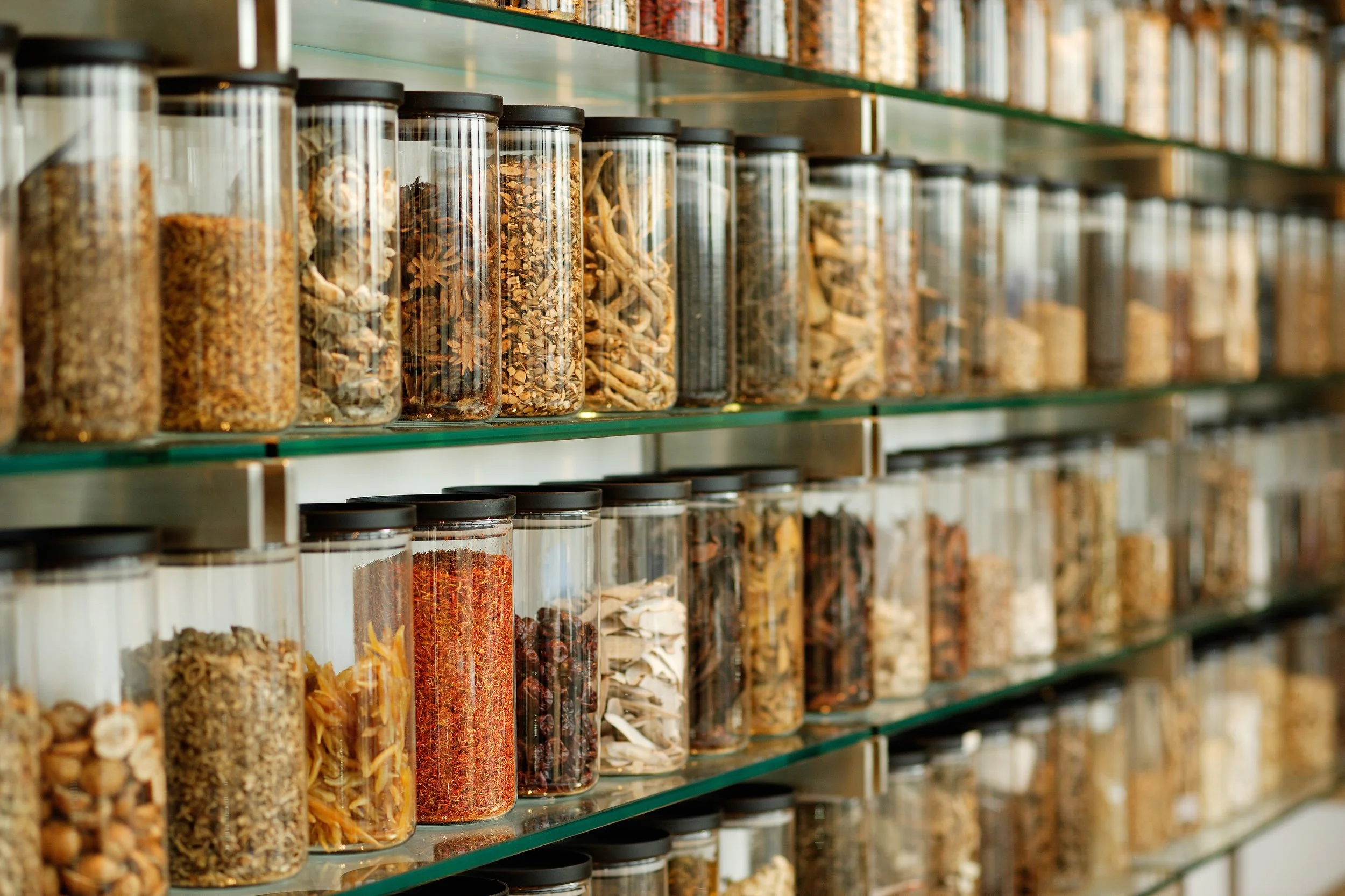 Glass jars filled with dried herbs and spices on metal shelves in a spice shop.