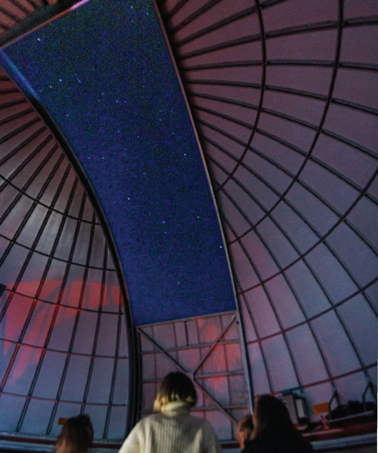 People inside an observatory looking up at the night sky with a telescope