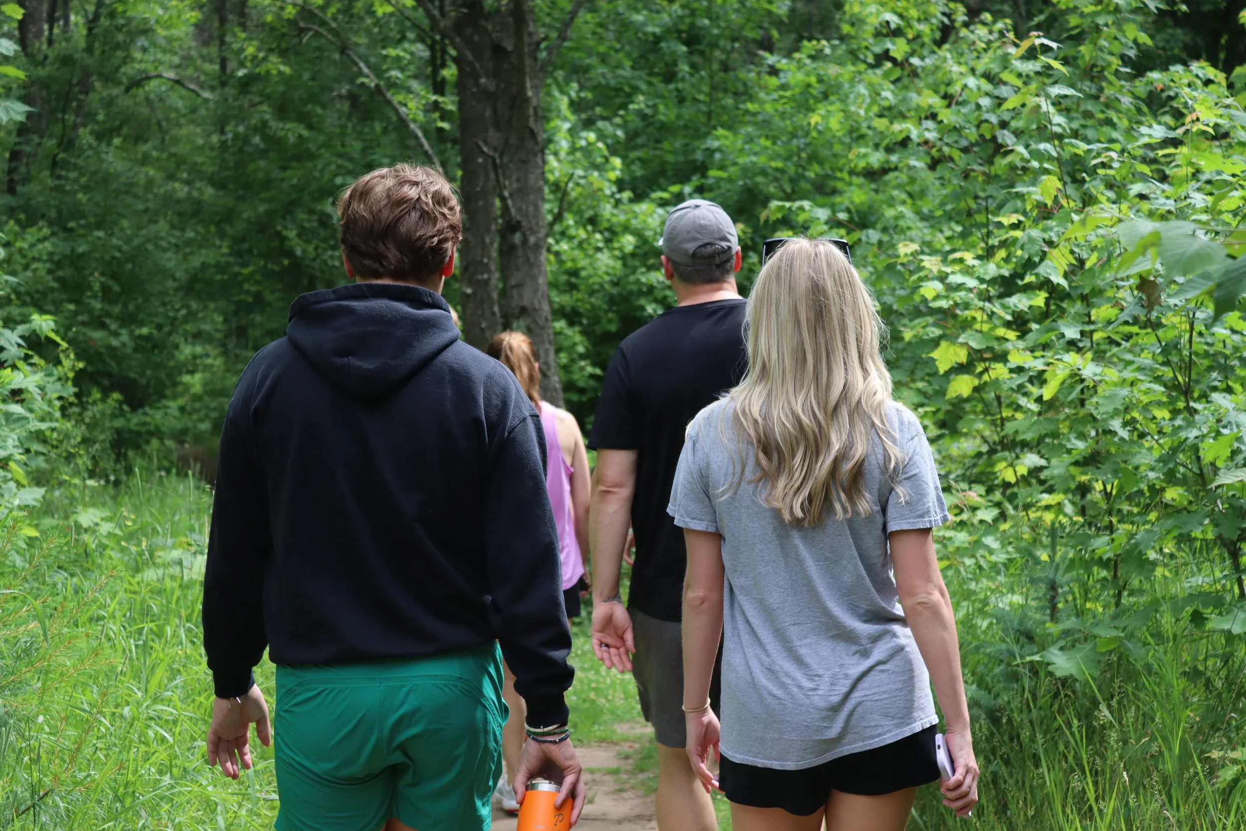 Group of young people walking on a trail through a green, leafy forest.