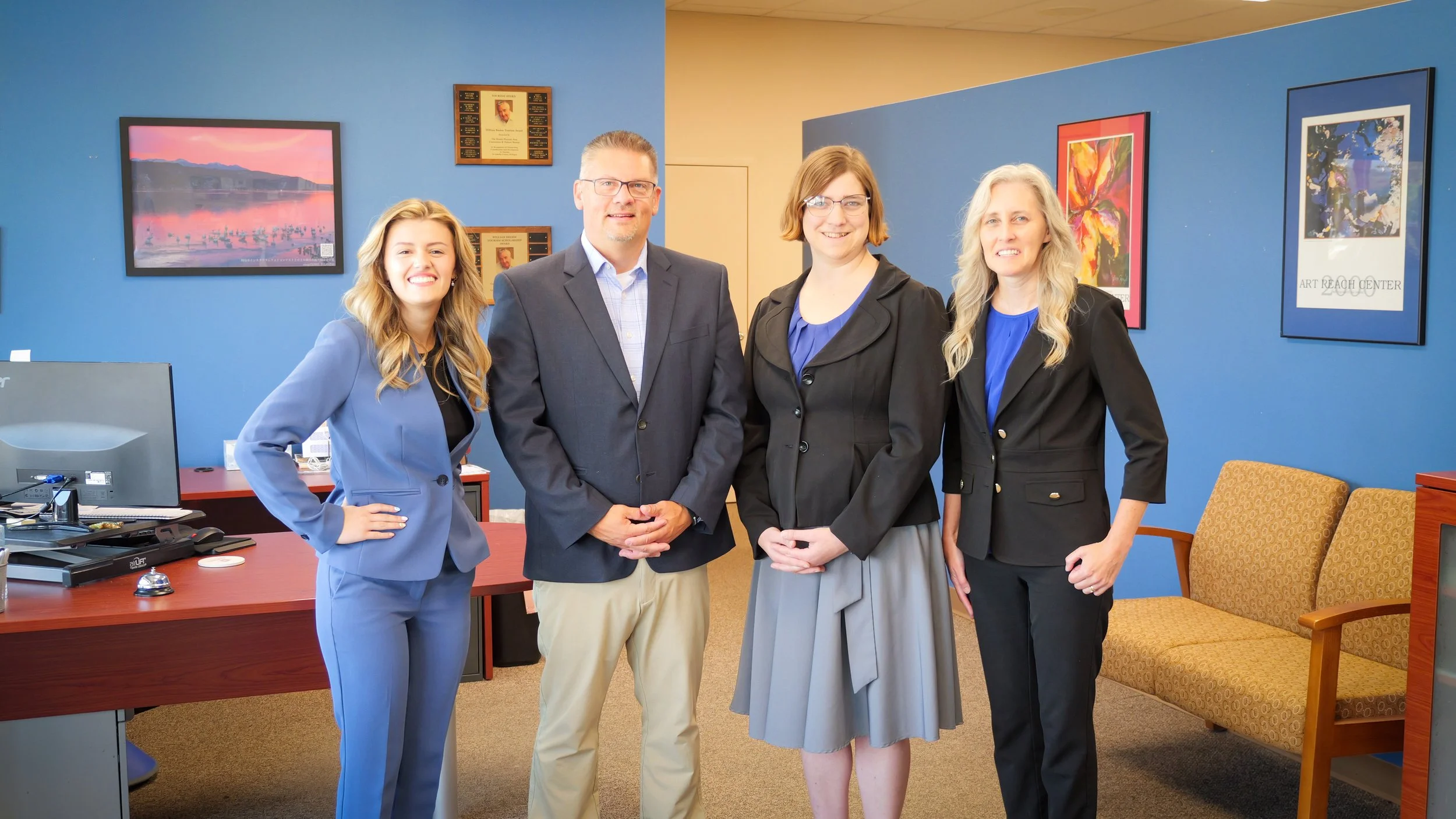 Four professionals standing in an office, smiling, with colorful artwork on blue walls behind them