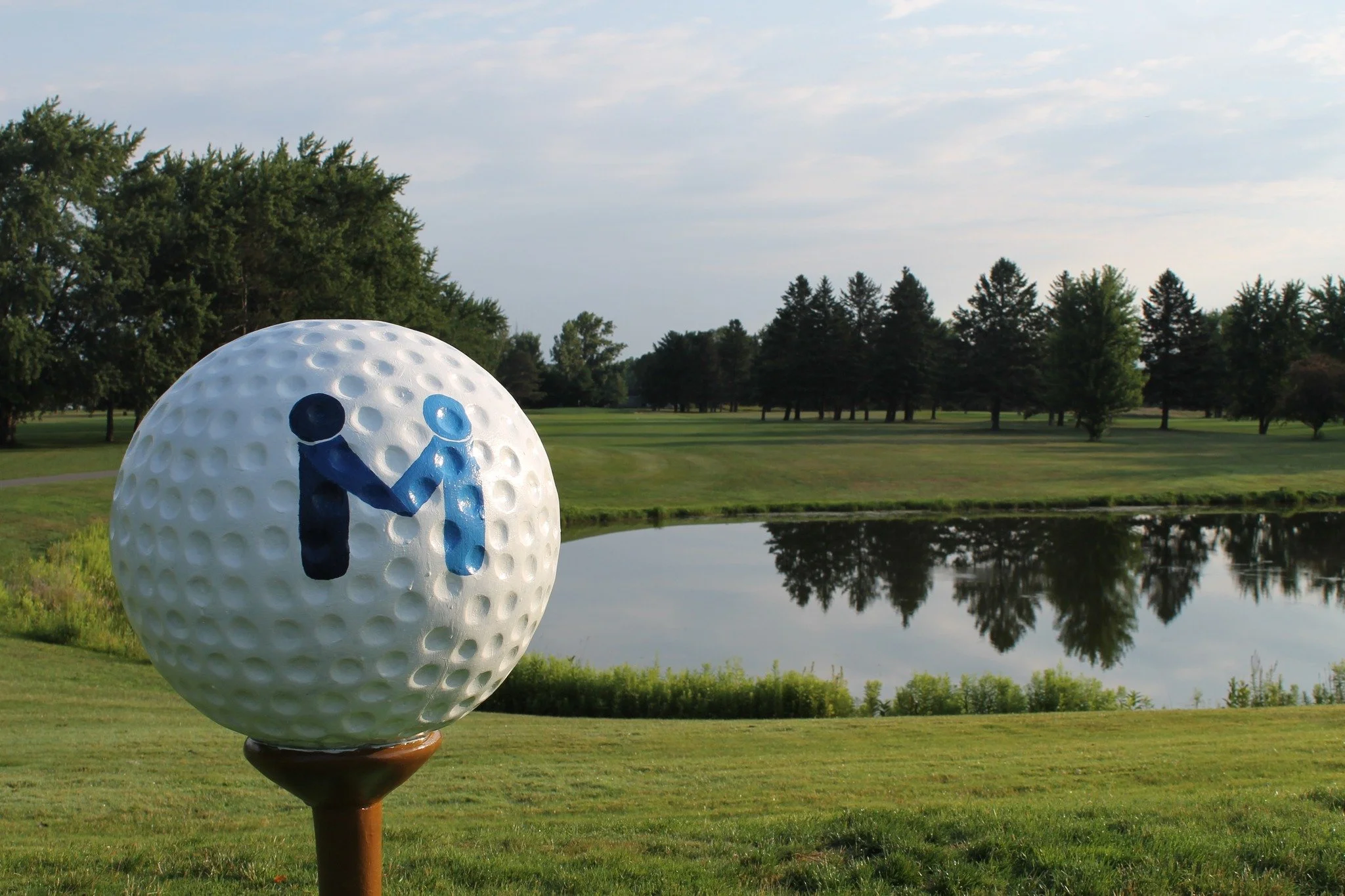 Giant golf ball with a blue M on a golf course