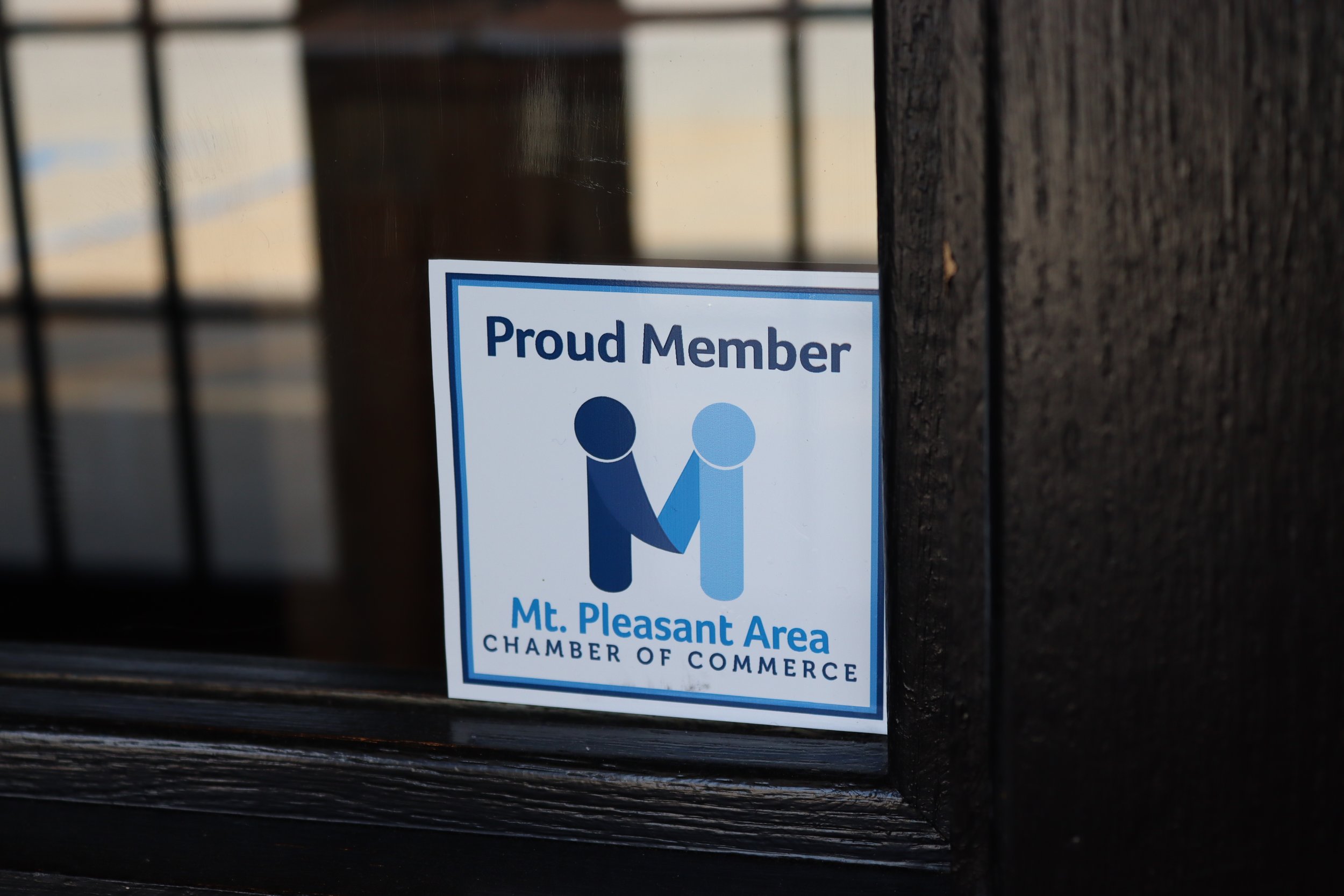 A sticker on a window that says 'Proud Member Mt. Pleasant Area Chamber of Commerce' with an icon of two figures shaking hands.