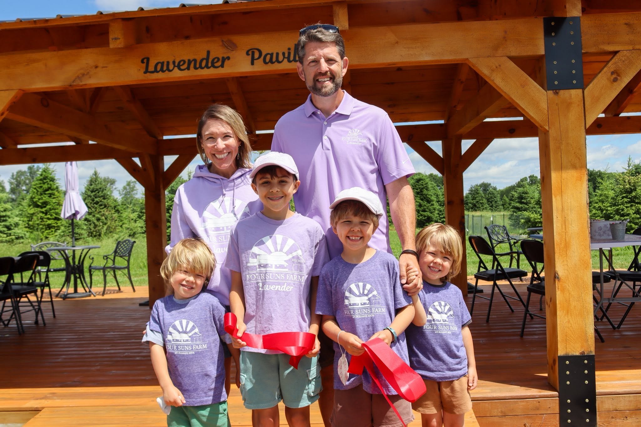 A woman and man with four boys all in lavender t-shirts standing in front of a pavilion smiling