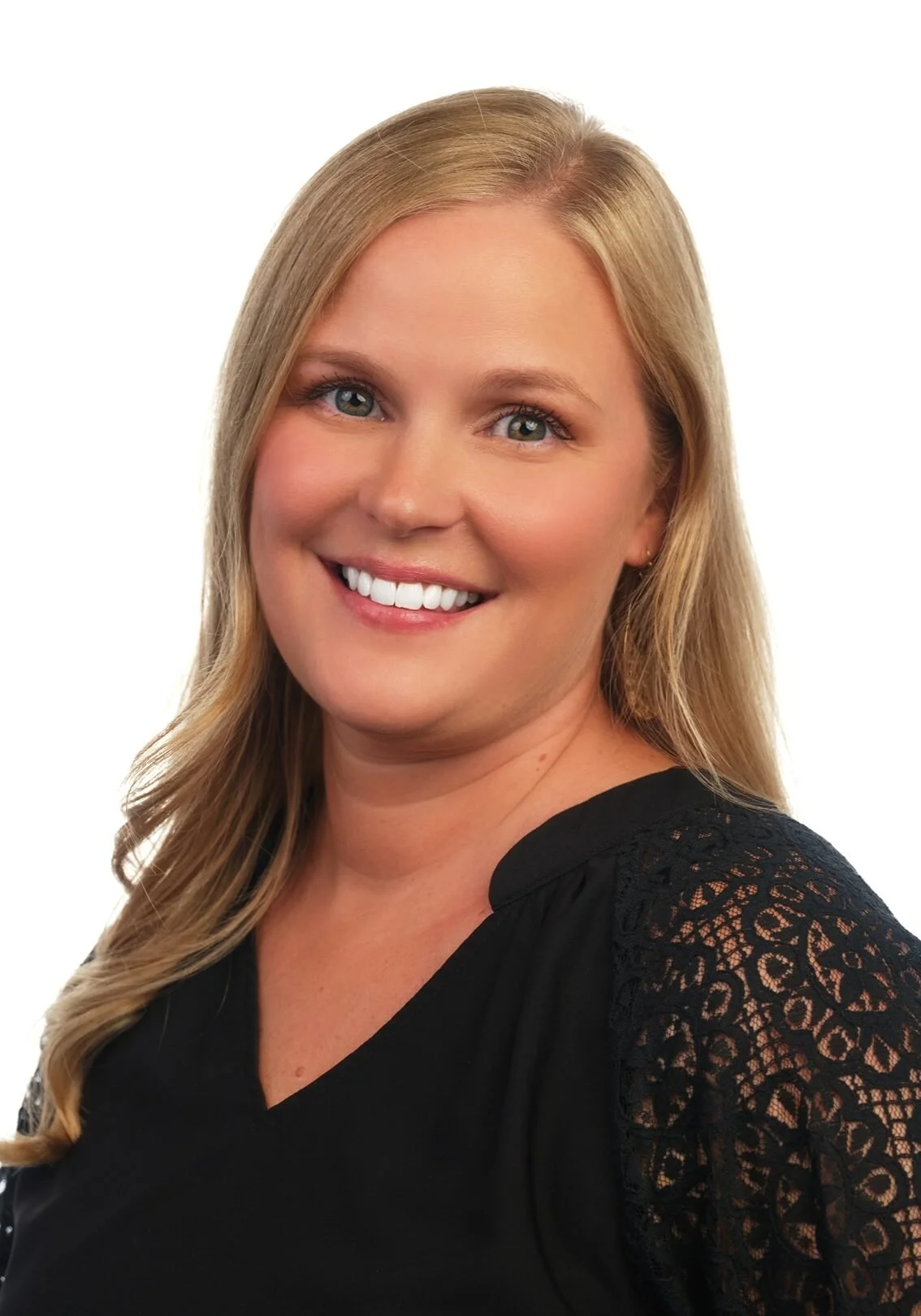Portrait of a smiling woman with blonde hair, blue eyes, wearing a black top with lace details on the sleeves.