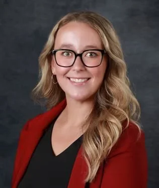 A blonde woman smiling with a red blazer black shirt and black glasses