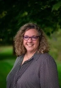A woman with short curly hair standing outside smiling