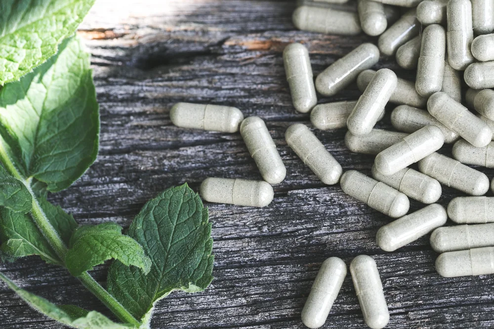 Herbal capsules and mint leaves on a wooden surface