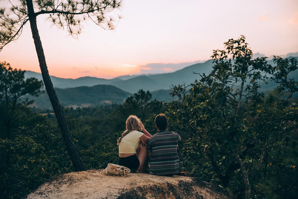 Two people looking across a mountain landscape at sunset