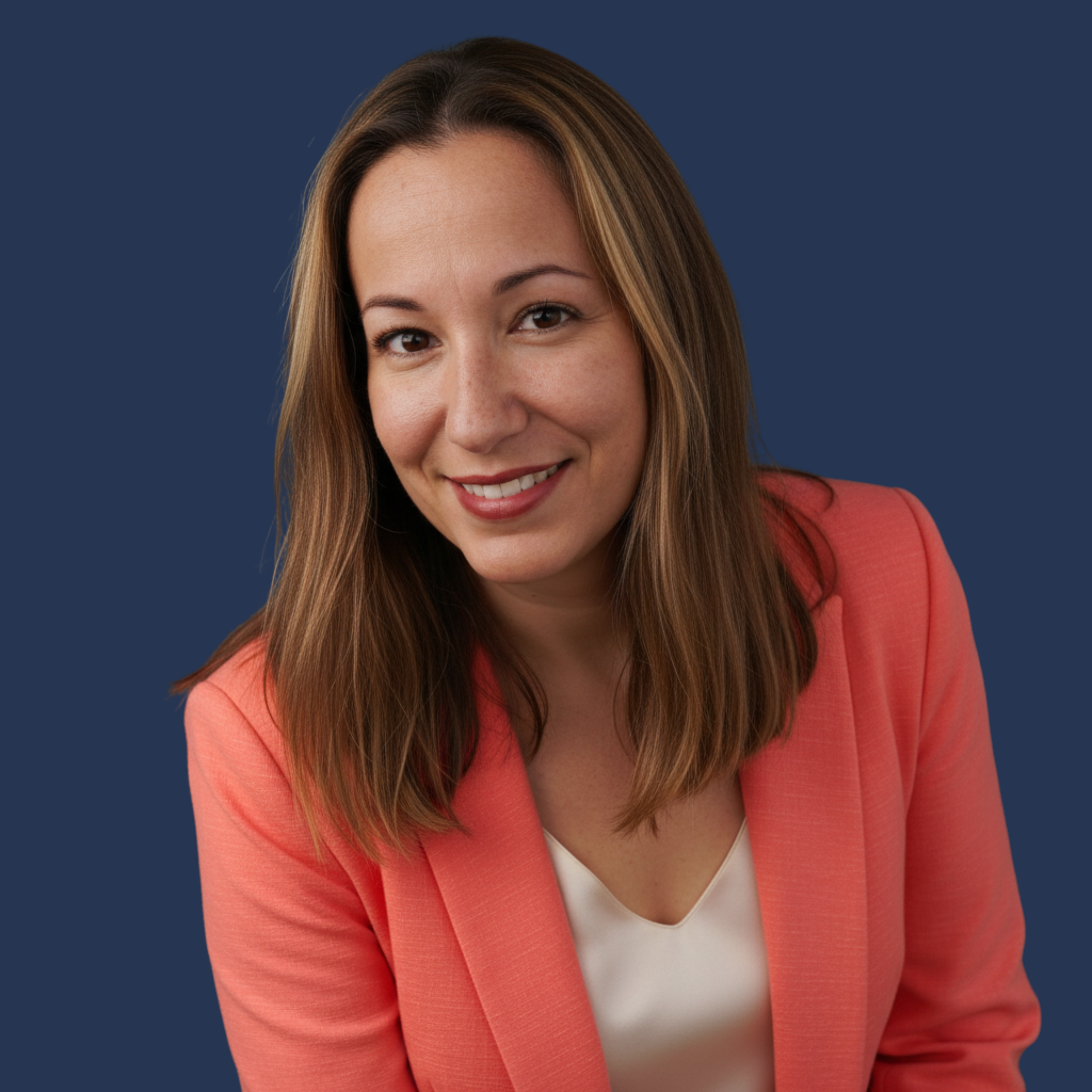 A woman with brown hair and a warm smile, wearing a coral blazer and white top, standing against a dark blue background.