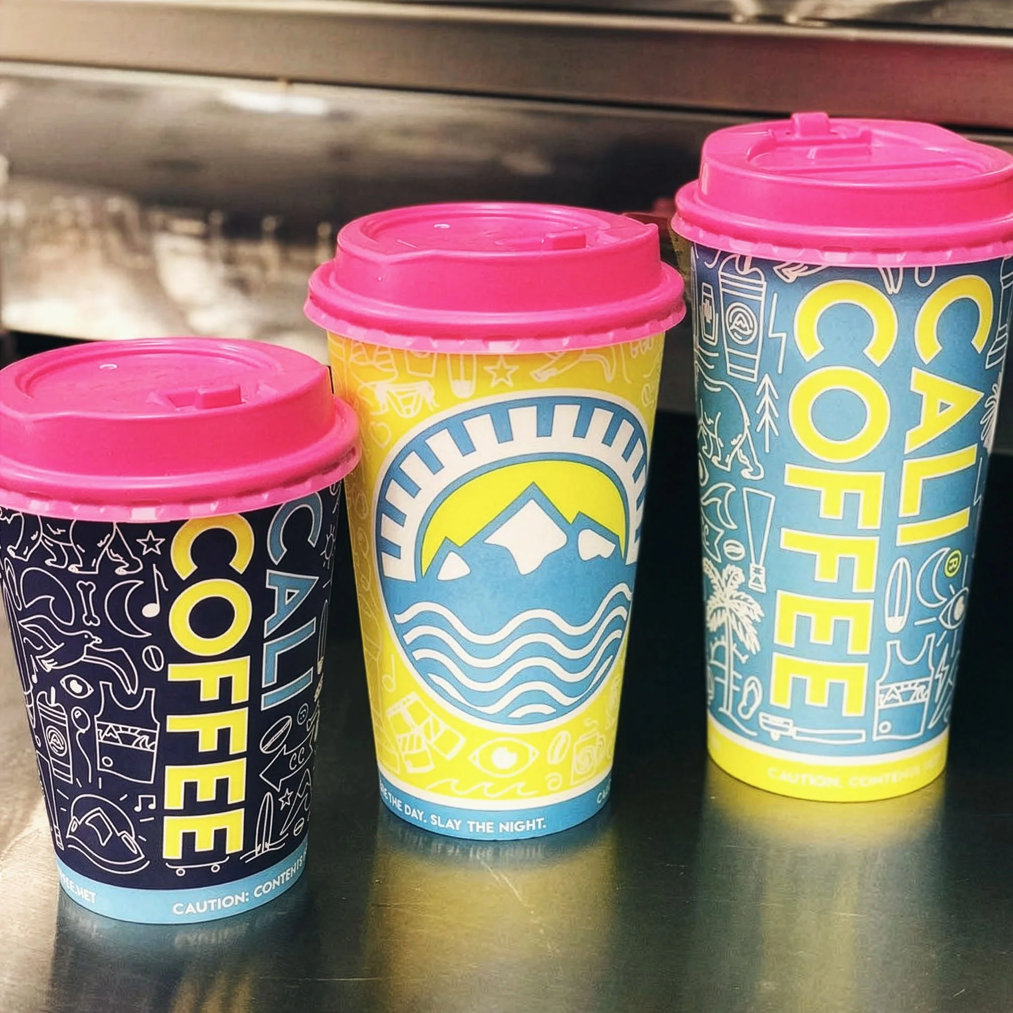 Three sizes of Cali Coffee hot cups with custom Iconoflage pattern in black, yellow, and blue colorways