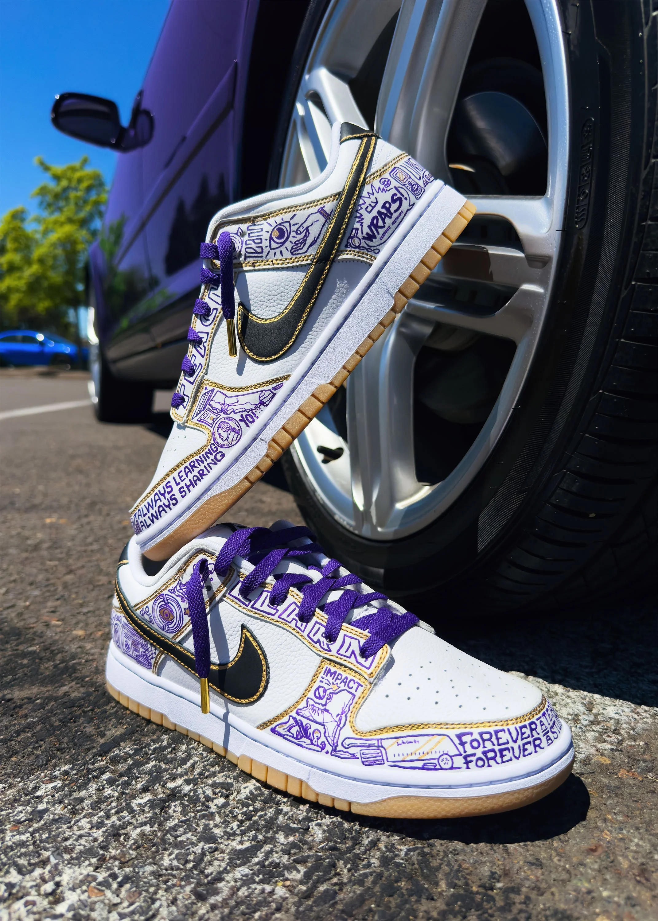 Hand-painted Nike Dunks featuring entrepreneurial icons propped against luxury car wheel