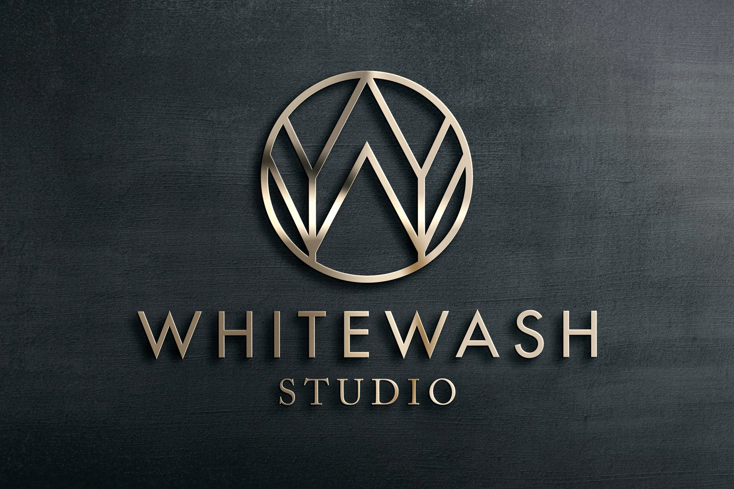 Whitewash Studio brand lockup on dimensional brushed metal sign mounted on dark wall