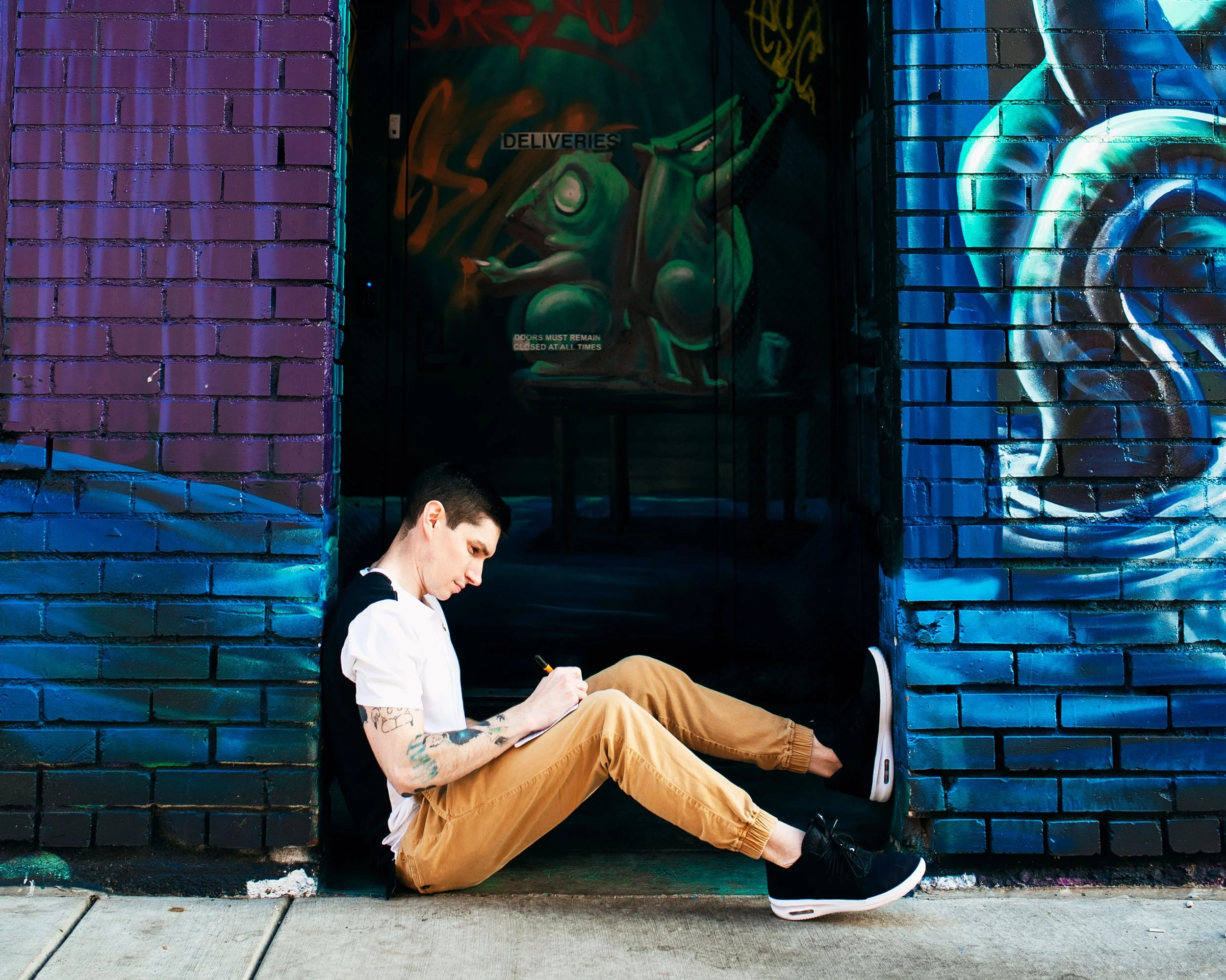 Scott Hofford sketching in notebook against vibrant geometric mural background