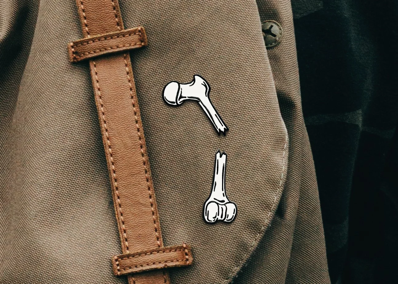 White broken bone enamel pins attached to tan canvas backpack with leather straps