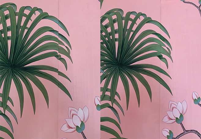 Close-up of de Gournay large green tropical plant with long, pointed leaves against a pink wall with painted flowers.
