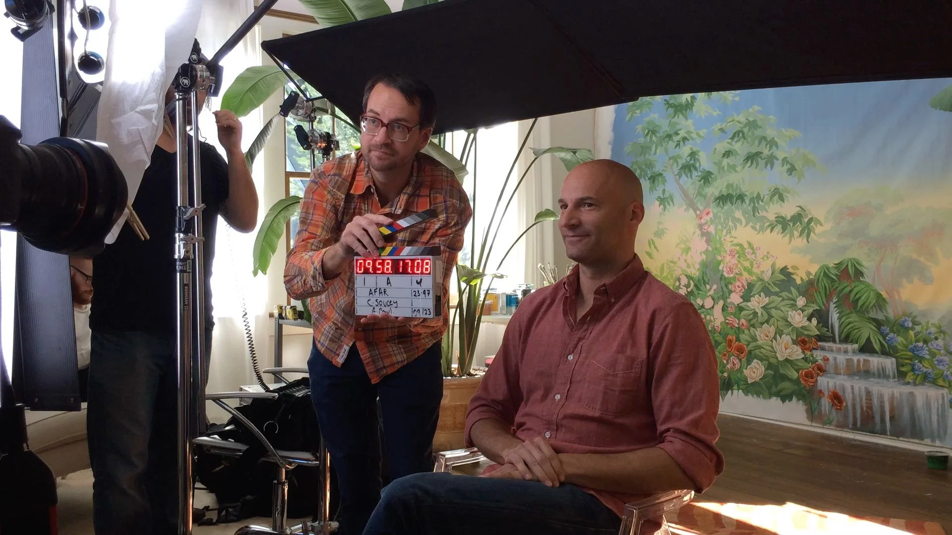 Film crew filming a scene of Andrew Tedesco in his art Studio sitting in front of a painted backdrop of a lush garden with waterfalls.