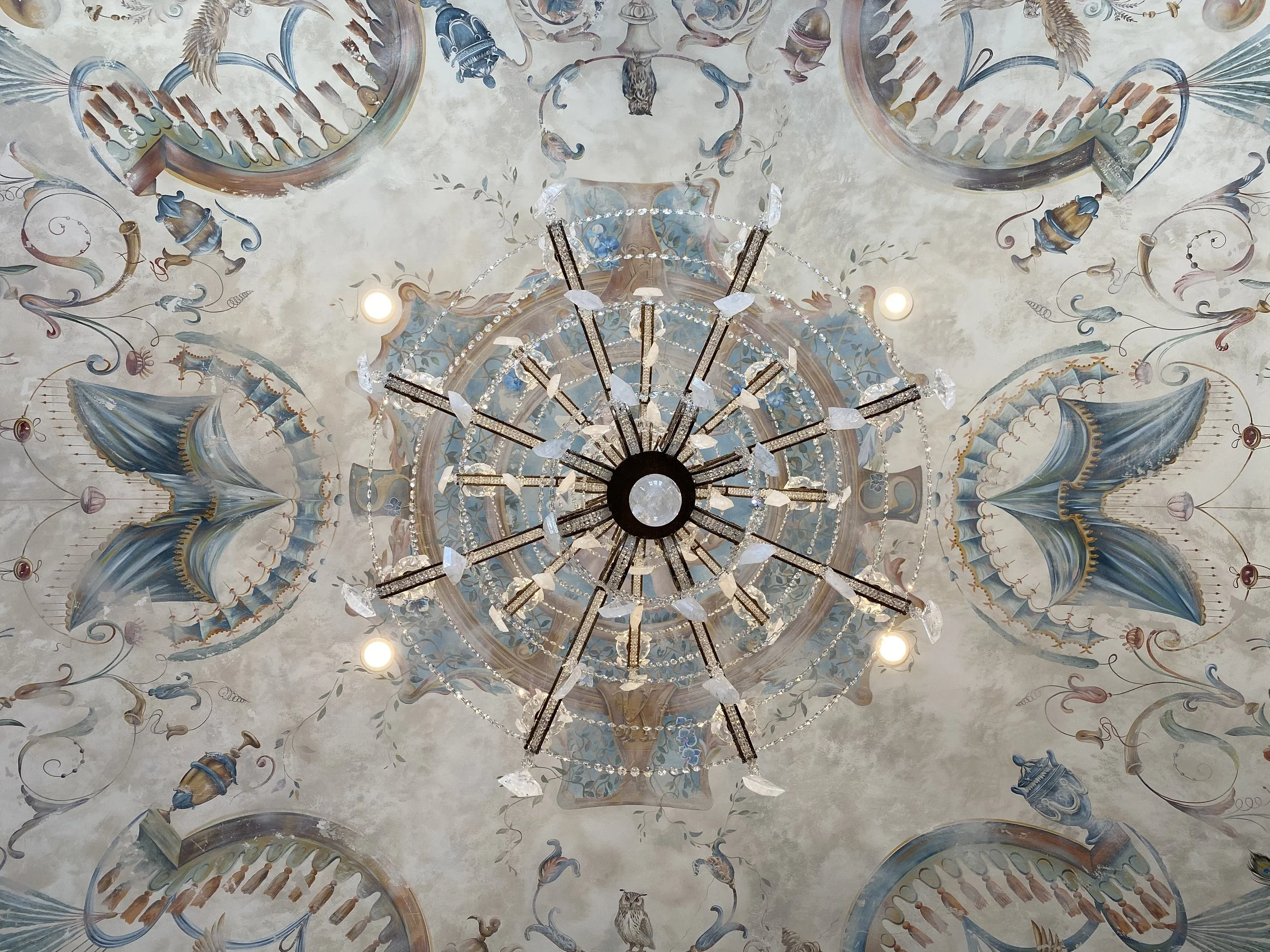 Decorative ceiling mural in Orange County California with painted motifs and a central chandelier with multiple glass crystals.
